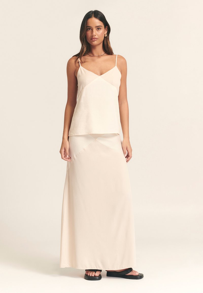 Heled helebeežist kamsüül õhukeste rihmadega, mille all on sobiv maksikleit. Kangas tundub sile ja kerge sädeleva läikega, sisaldades minimaalset disaini.