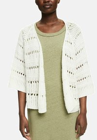Cárdigan blanco de punto con patrón de tricotado abierto y mangas anchas, usado sobre un vestido verde claro. La textura es suave y transpirable.