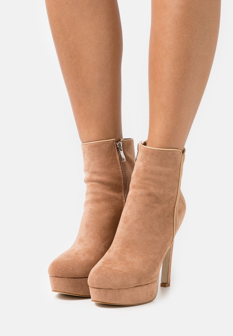 Bottines beige en daim avec une plateforme haute et un talon stiletto, dotées d'une fermeture éclair latérale et d'une texture lisse.