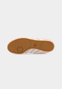 Σόλα ροζ αθλητικού παπουτσιού Adidas με καφέ υφή λαβής και λευκές ρίγες, εμφανίζοντας το λογότυπο Adidas στο κέντρο της σόλας.