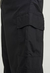 Pantaloni cargo neri realizzati in un tessuto leggero con molteplici tasche e una vestibilità rilassata. Cuciture visibili e texture morbida.