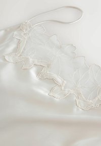 Silk camisole in cream with delicate lace trim featuring floral embroidery along the top edge. Adjustable straps complete the design.