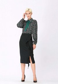 Blouse florale à manches longues avec un nœud en ruban vert, assortie à une jupe noire à ourlet volanté et fente sur le côté. Escarpins noirs.