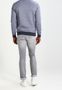 Jeans grigi con una vestibilità slim, orli arrotolati e due tasche posteriori; abbinati a una felpa blu strutturata con un orlo scuro.