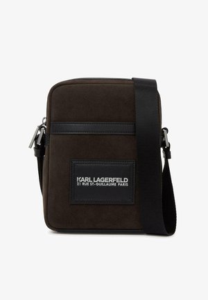 Barna textil keresztpántos táska sima fekete bőr szegéllyel, elöl logóval ellátott plakettel és állítható pánttal. Téglalap alakú.