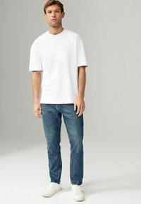 Tricou alb din bumbac cu mâneci scurte, asociat cu blugi negri și adidași albi. Design simplu, croială regulară, detalii minime.