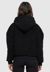 Black faux fur jacket with a hood, featuring a textured surface and ribbed cuffs. The design is boxy with a cropped fit.