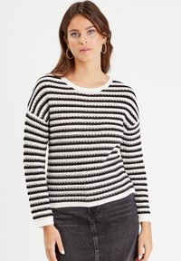 Black and white striped knitted sweater with a wide crew neckline and ribbed cuffs, paired with a black denim skirt.