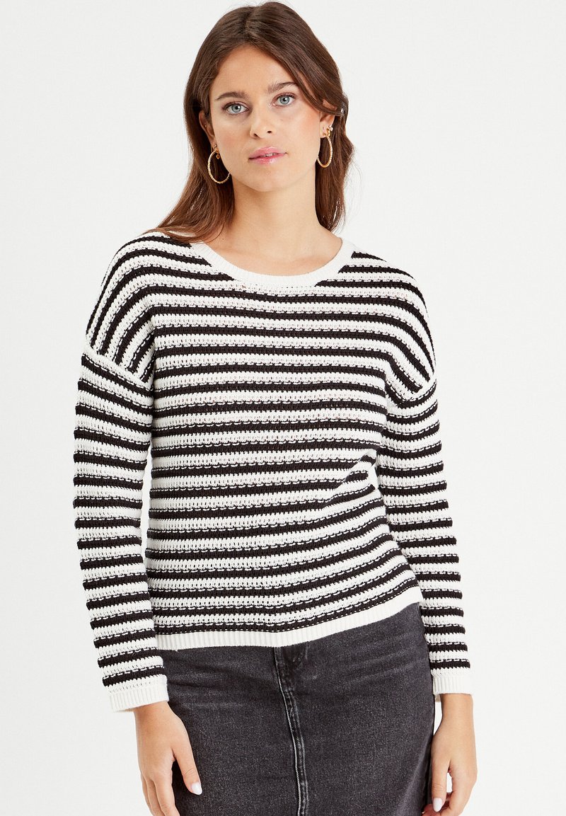 Black and white striped knitted sweater with a wide crew neckline and ribbed cuffs, paired with a black denim skirt.