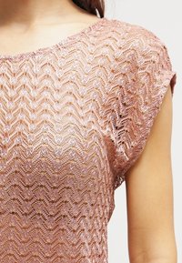 Světlounce růžový, průsvitný top s krátkými rukávy a vlnitým háčkovaným vzorem, s kulatým výstřihem a texturovaným povrchem.