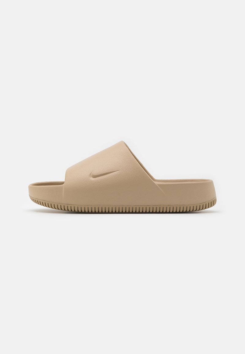 Sandales Nike slide beige clair, en caoutchouc moulé, avec une large bride et une semelle texturée, ornées d'un petit logo sur la partie supérieure.