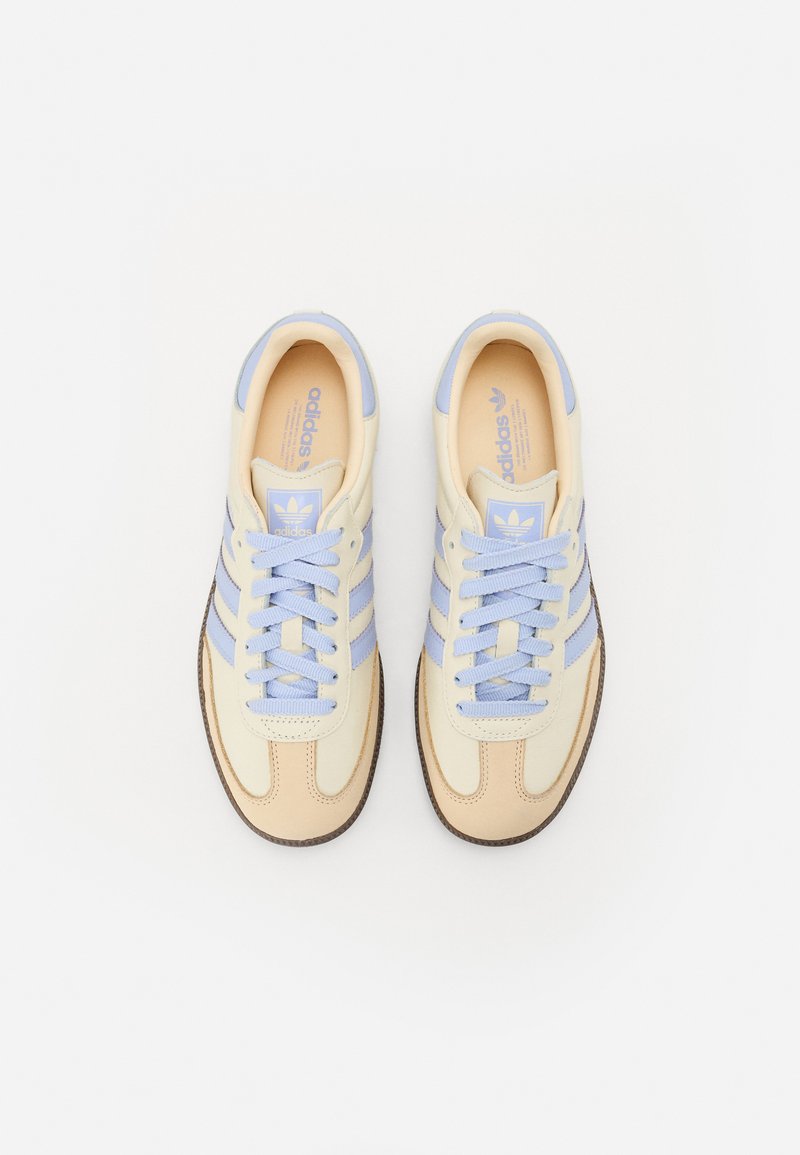 Beige en lichtblauwe sneaker met drie blauwe strepen, beige accenten, ronde neus en gestructureerde rubberen zool. Heeft blauwe veters en branding.
