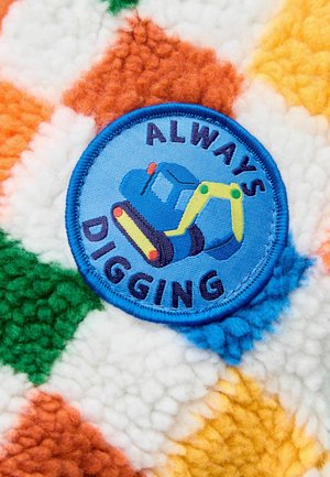 Kék hímzett folt, rajta az "ALWAYS DIGGING" felirattal, texturált plüss anyagon, narancs, zöld, sárga és fehér gyémántmintákkal.