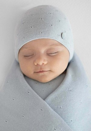 Bébé endormi emmailloté dans une couverture tricotée gris clair et portant un chapeau assorti avec des détails texturés et un petit bouton.