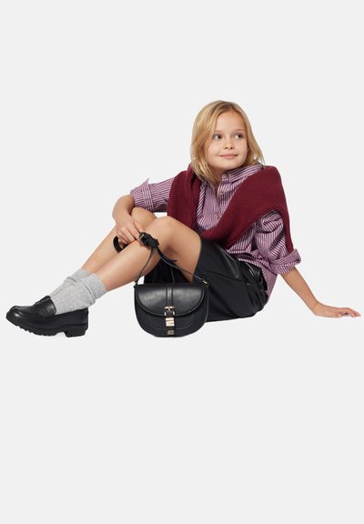 Sac à main en cuir noir avec détails en métal doré. Porté avec un pull en maille bordeaux sur une chemise rayée et une jupe noire, complété par des chaussettes grises et des chaussures noires.