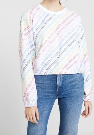 Biała krótka bluza z długim rękawem z wielokolorowym ukośnym wzorem tekstowym "Fitch Abercrombie", zestawiona z wysokim stanem niebieskich dżinsów.