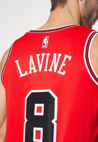 Punainen koripallopaita mustilla ja valkoisilla yksityiskohdilla. Selkäpuolella on nimi "LAVINE" ja numero "8" paksulla valkoisella kyllä. NBA-logo näkyvissä.