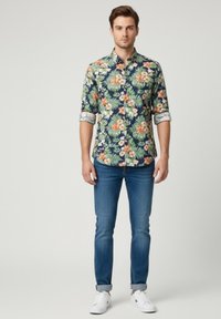 Camisa de botones con estampado floral sobre fondo azul marino, que presenta patrones en rosa brillante y verde; combinada con jeans ajustados azules y zapatillas blancas.