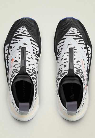 Čierne a biele športové topánky s dizajnom leopardích škvrn, hladký textilný zvršok a odolná gumová podrážka. Obsahujú pútko na päte.