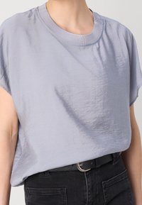 Světle levandulové tričko s krátkým rukávem vyrobené z měkké, strukturované tkaniny s kulatým výstřihem, nošené s černými džíny s vysokým pasem a černým opaskem.