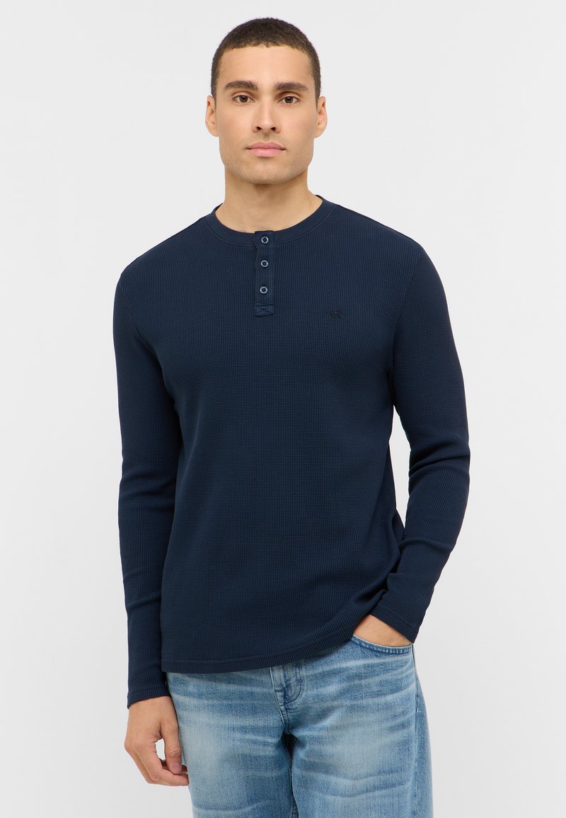 Navy long-sleeve henley shirt in ribbed texture, featuring a round neckline and three-button placket, paired with light blue jeans.