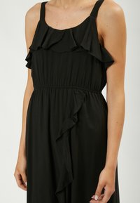 Abito nero senza maniche con scollatura arricciata e vita elastica. Tessuto morbido con una silhouette fluida e dettagli di ruffle laterale.