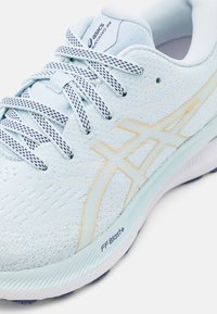 Chaussure de course Asics Kayano 29 bleu clair avec lacets blancs et bleu marine et marquage sur le côté et la semelle intermédiaire.