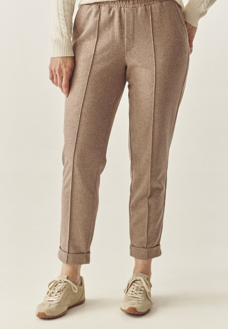 Light brown, textured tapered pants with an elastic waistband, side seams, and rolled cuffs, paired with beige sneakers.