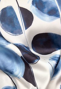 Seidenstoff mit großen, abstrakten blauen und schwarzen kreisförmigen Mustern auf einem cremfarbenen Hintergrund, mit einer glatten, glänzenden Textur.