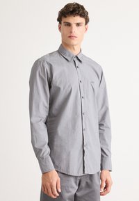 Camicia grigia con colletto, maniche lunghe e una texture liscia. Presenta bottoni abbinati e un logo discreto sul petto.