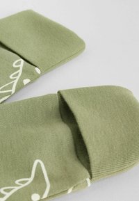 Chaussettes vert clair avec une texture douce et un motif abstrait blanc près de la cheville, dotées d'un haut côtelé et d'une finition en tissu lisse.