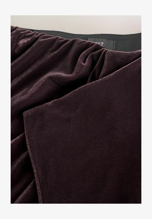 Mörklila sammetstyg med en mjuk textur, som har samlad detalj och en ren kant, uppvisad mot en ljus bakgrund.
