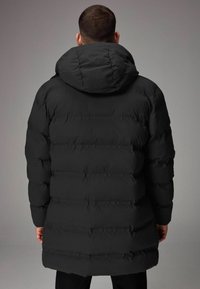 Chaqueta acolchada negra con capucha, que presenta secciones acolchadas y una textura suave. El diseño es largo, lo que proporciona una cobertura completa.