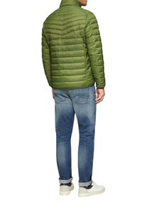 Olivenfarbene Daunenjacke mit gestepptem Muster, hohem Kragen, kombiniert mit blauen, verwaschenen Jeans und weißen Turnschuhen. Lässige Freizeitkleidung.