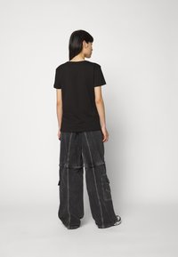 T-shirt en coton noir associé à un pantalon cargo large de couleur gris foncé avec un design à double couche, des poches avant et des détails de couture visibles.