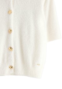 Kræmfarvet, fluffy cardigan med fire guldtonede, klippeformede knapper og et lille mærke ved kanten.