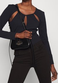 Svart långärmad topp med utskärningar, tillsammans med svarta högmidjade jeans och en liten svart handväska med ett silverlås.