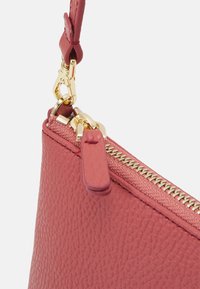 Angolo di borsa in pelle rosa con una cerniera dorata, caratterizzata da una finitura testurizzata, accessori in metallo e un tirante in pelle.