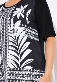 Top en blanco y negro con un estampado botánico. Mangas cortas, escote redondo y un patrón texturizado con hojas y diseños geométricos.