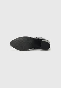 Suela de zapato de piel negra con forma puntiaguda, patrón de agarre de goma texturizada y acentos lisos. Logotipo impreso cerca de la zona del talón.