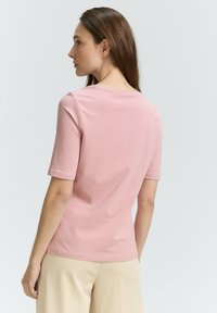 Rosa Baumwoll-T-Shirt mit kurzen Ärmeln, rundem Ausschnitt, glatter Textur und schlichtem Design, von hinten gezeigt.