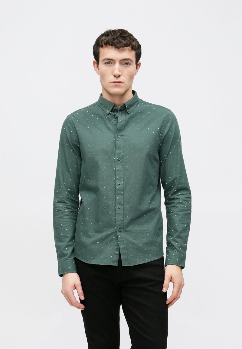 Grünes Langarmhemd mit einem Button-Down-Kragen, das ein dezentes Muster aus kleinen hellblauen Punkten aufweist und aus einem glatten Stoff gefertigt ist.