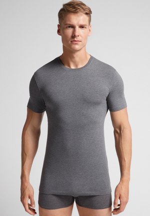 Camiseta gris de manga corta en tejido suave, diseño ajustado y cuello redondo. Combinada con pantalones cortos grises a juego. Textura suave y detalles mínimos.