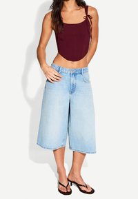 Burgundské krátké triko s dvěma šňůrkami, spárované s světle modrými širokými džínami. Sandály mají tenký černý řemínek a blokový podpatek.