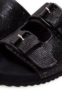 Zwarte sandalen met een textuur bovenkant, voorzien van kleine studs, twee verstelbare gespbanden en een zachte zwarte zool.