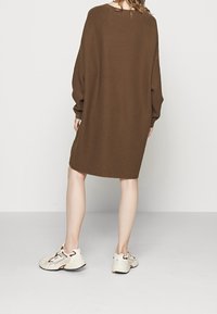 Brun ribbad oversize tröjklänning med långa ärmar och rund halsringning. Avslappnad passform som når till mitten av låret, kombinerad med ljusa sneakers.