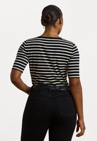 Černobíle pruhovaný krátký rukáv top s kulatým výstřihem, který je kombinován s černými džíny s vysokým pasem a splétaným černým opaskem.