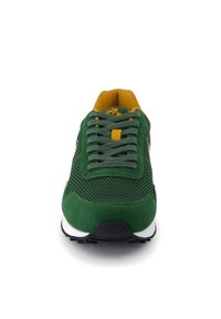 Scarpa da atletica verde con tomaia in mesh, dettagli in camoscio, lacci tondi, linguetta gialla e suola in gomma nera con intersuola bianca.