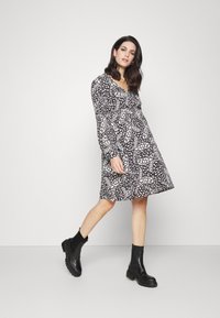 Vestido padrão preto e branco com mangas longas e saia rodada, combinado com botas ankle pretas. Textura suave e design em forma de v.