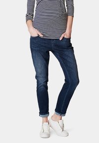 Mörkblå denimjeans med en avslappnad passform, med subtil blekning, framfickor och uppvikta fållar, kombinerat med vita sneakers.